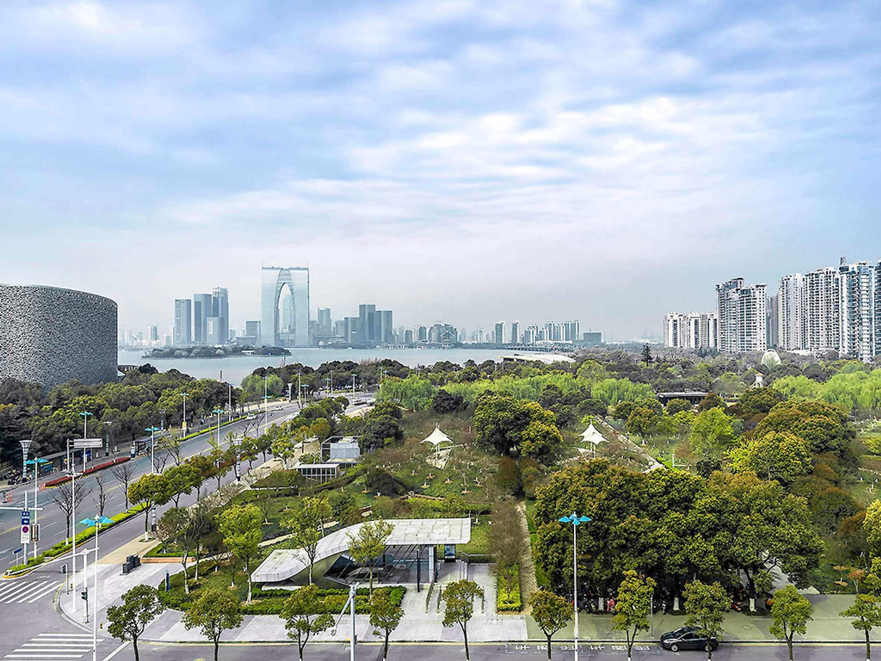 A cityscape with modern buildings, a river, and a park with trees and a pavilion.