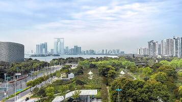 A cityscape with modern buildings, a river, and a park with trees and a pavilion.