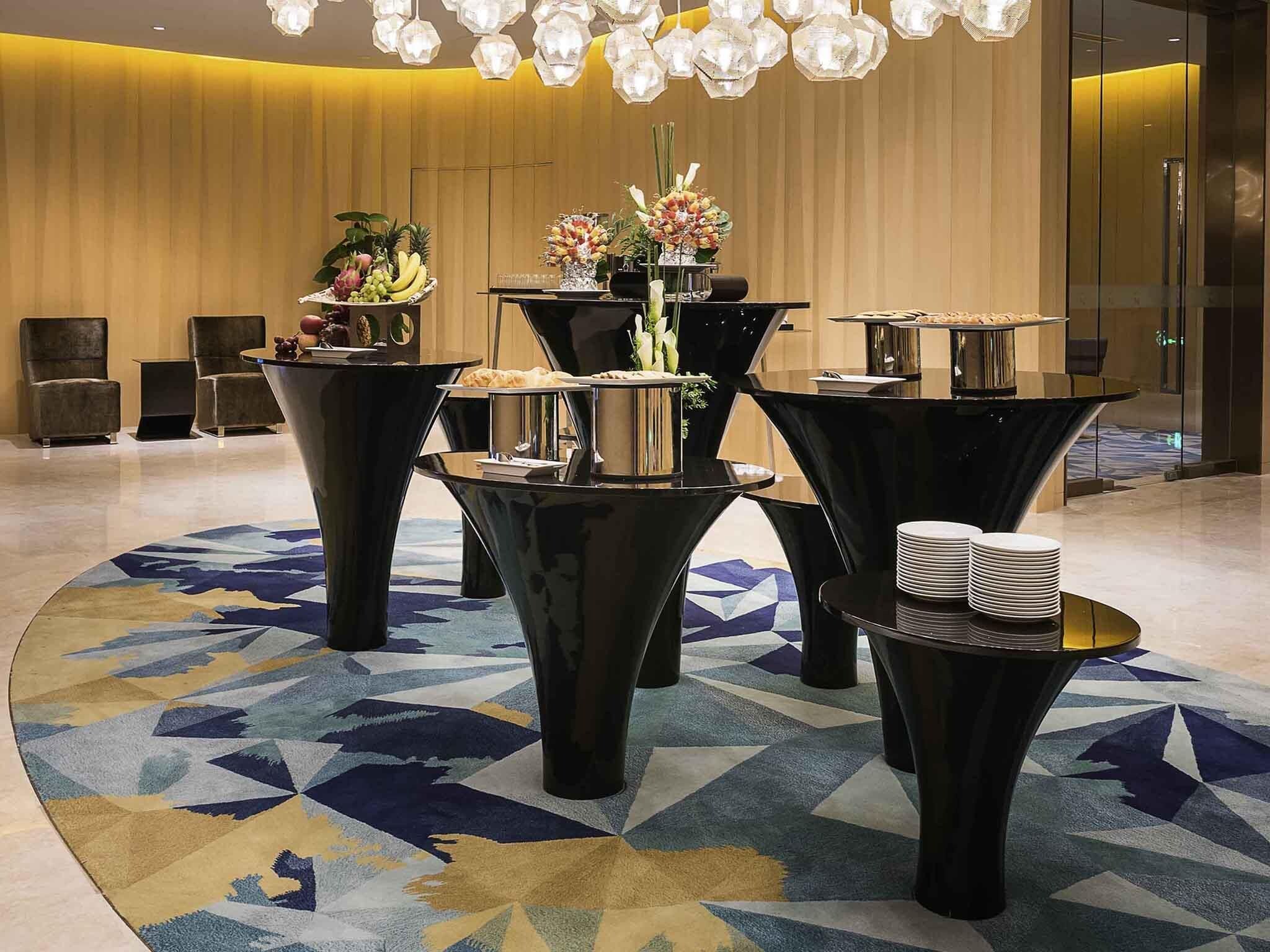 Un espace d’accueil avec plusieurs tables noires, dont certaines sont garnies de nourriture et de boissons, et un tapis à motifs.