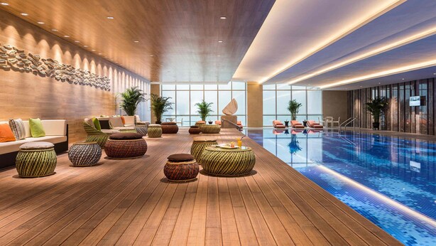 A modern indoor pool area with wooden flooring, seating arrangements, and a large window providing natural light. - Novotel Suzhou SIP (Suzhou)