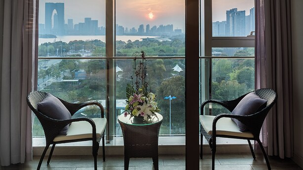A balcony with two wicker chairs and a table with flowers, overlooking a cityscape with a bridge and buildings. - Novotel Suzhou SIP (Suzhou)