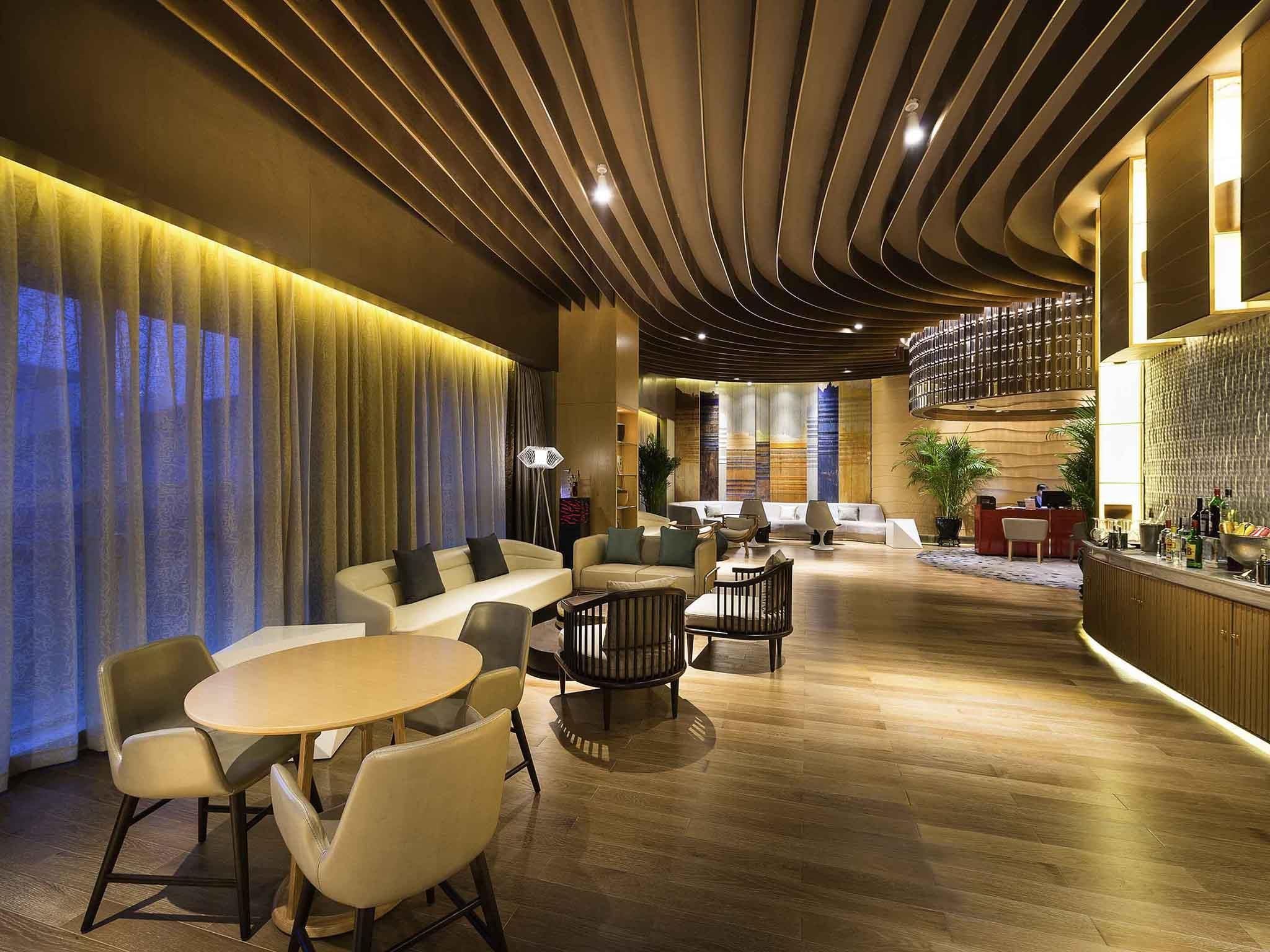 A modern hotel lobby with a central seating area, a bar, and a reception desk.
