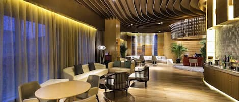 A modern hotel lobby with a central seating area, a bar, and a reception desk.