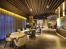 A modern hotel lobby with a central seating area, a bar, and a reception desk.