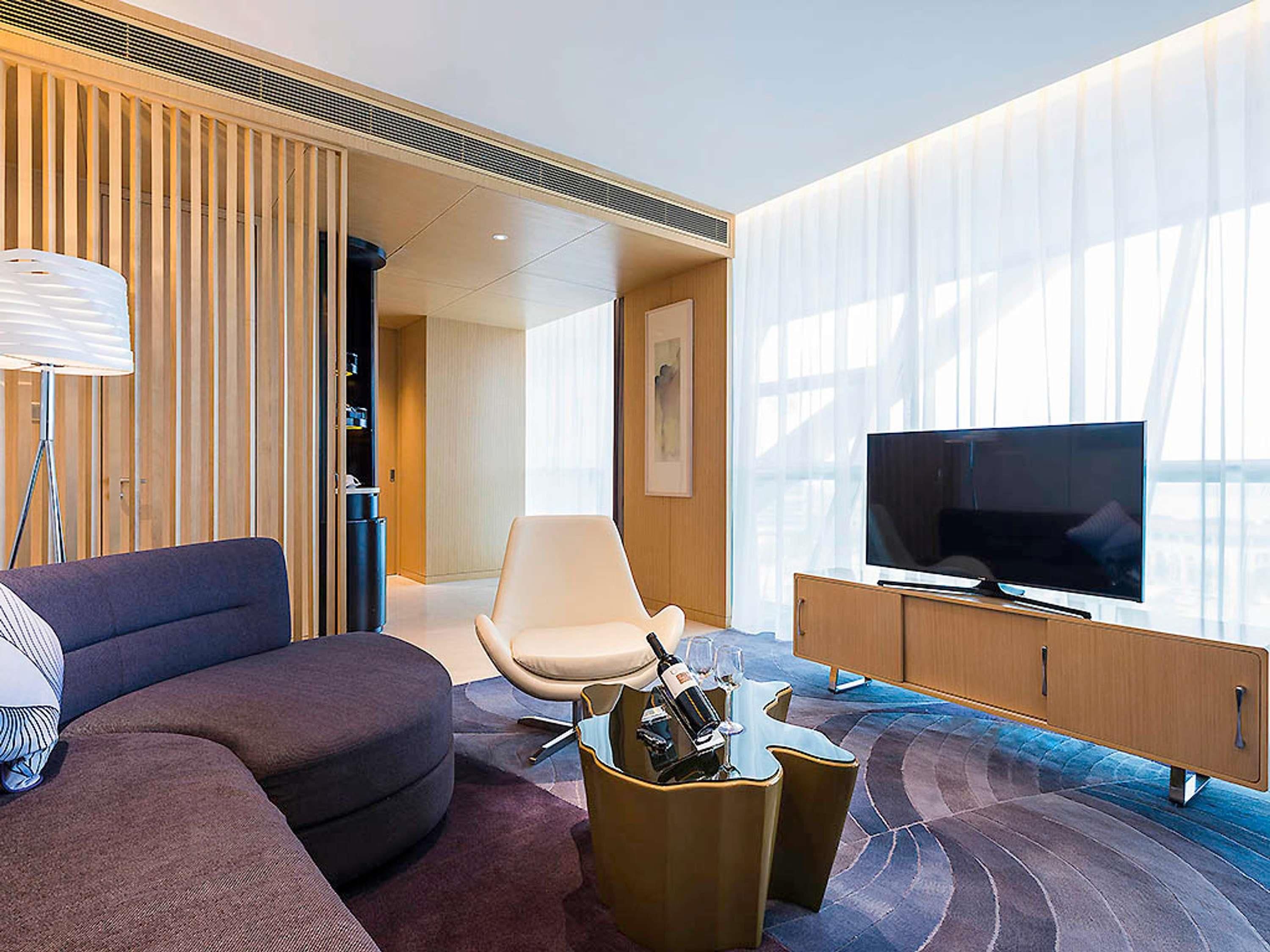 Habitació d'hotel moderna amb un sofà, una cadira, un televisor i una nevera petita.