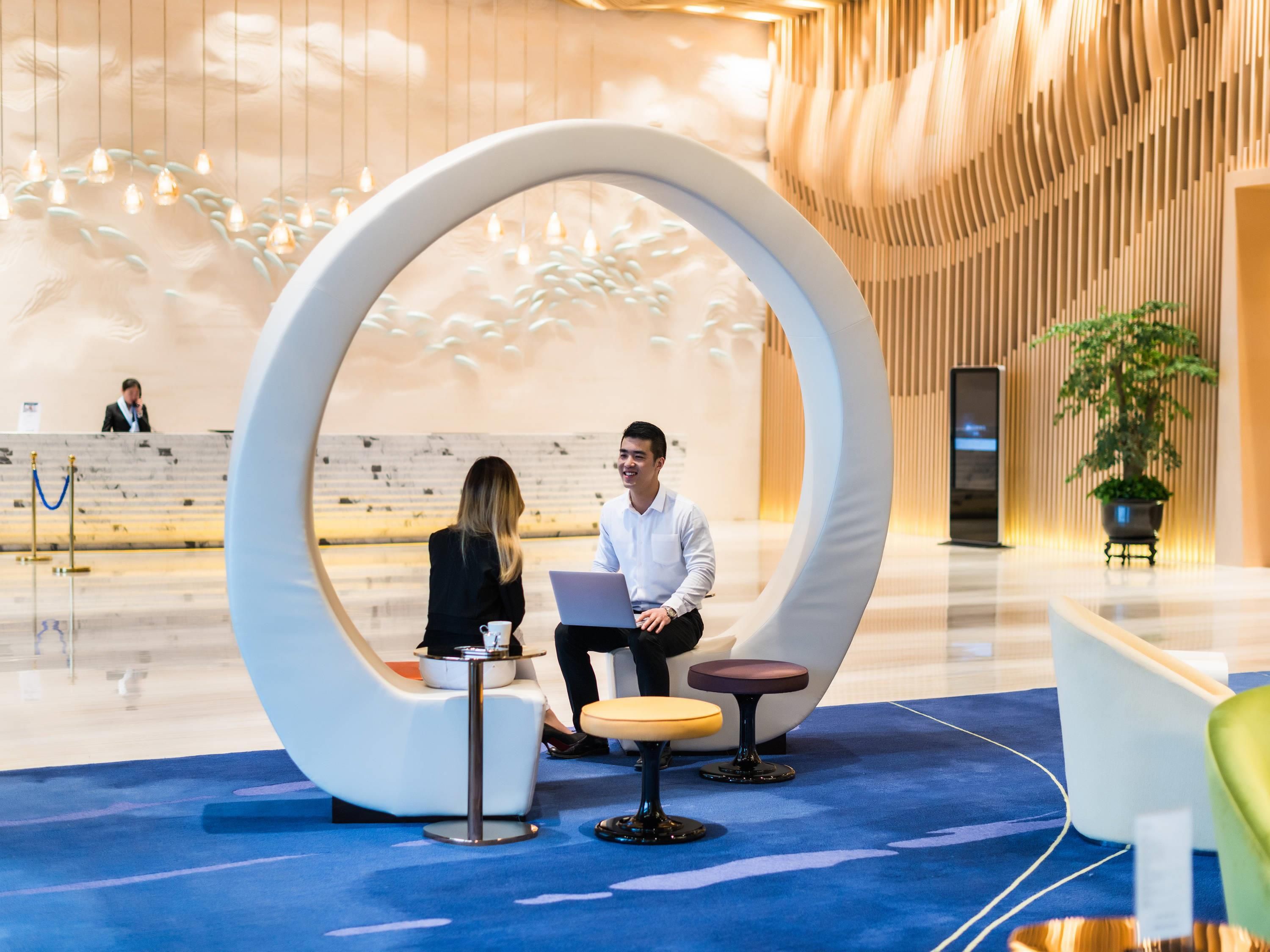 A modern reception area with a circular seating arrangement, a reception desk, and a potted plant.