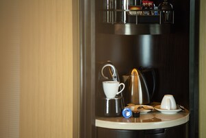 Una cafetera con taza y platillo, un hervidor y un plato pequeño con cuchara sobre una encimera.