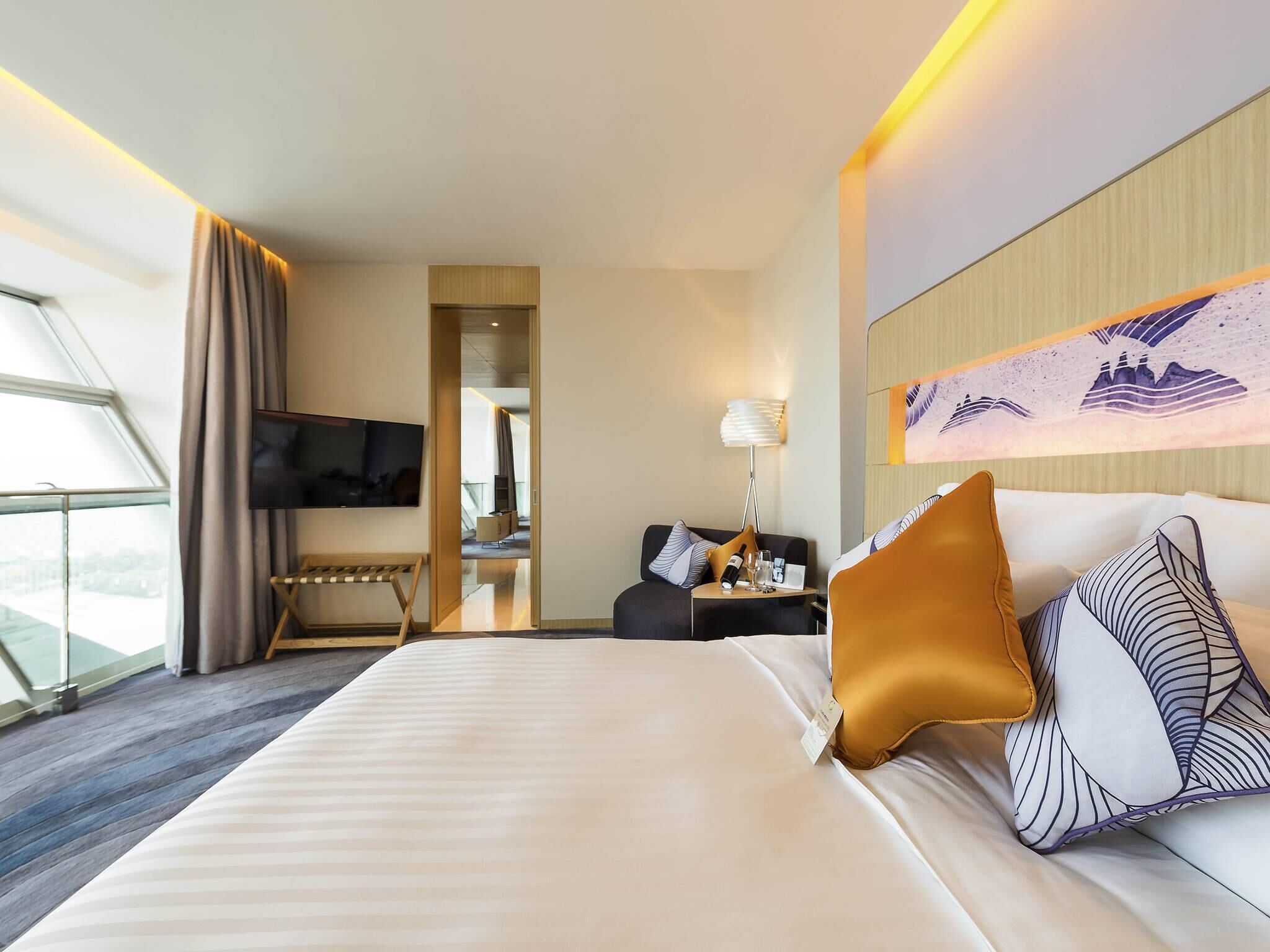 A hotel room with a bed, a TV, a desk, a lamp, and a view of the city.