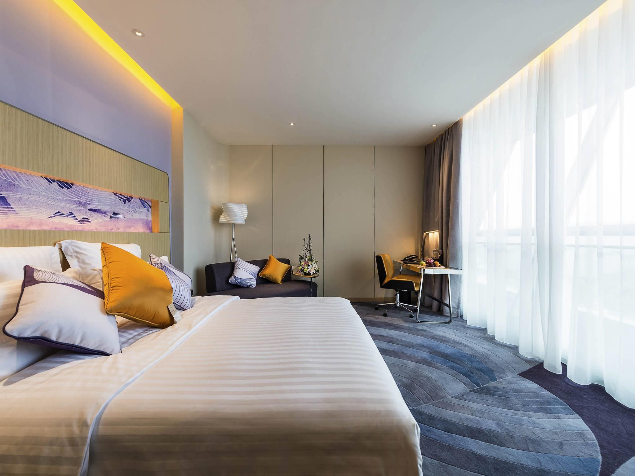 Habitación de hotel con una cama grande, un escritorio, una silla y una ventana con cortinas.