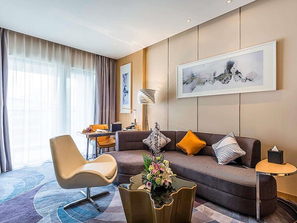 Una habitación de hotel moderna con sofá, sillón y zona de comedor.