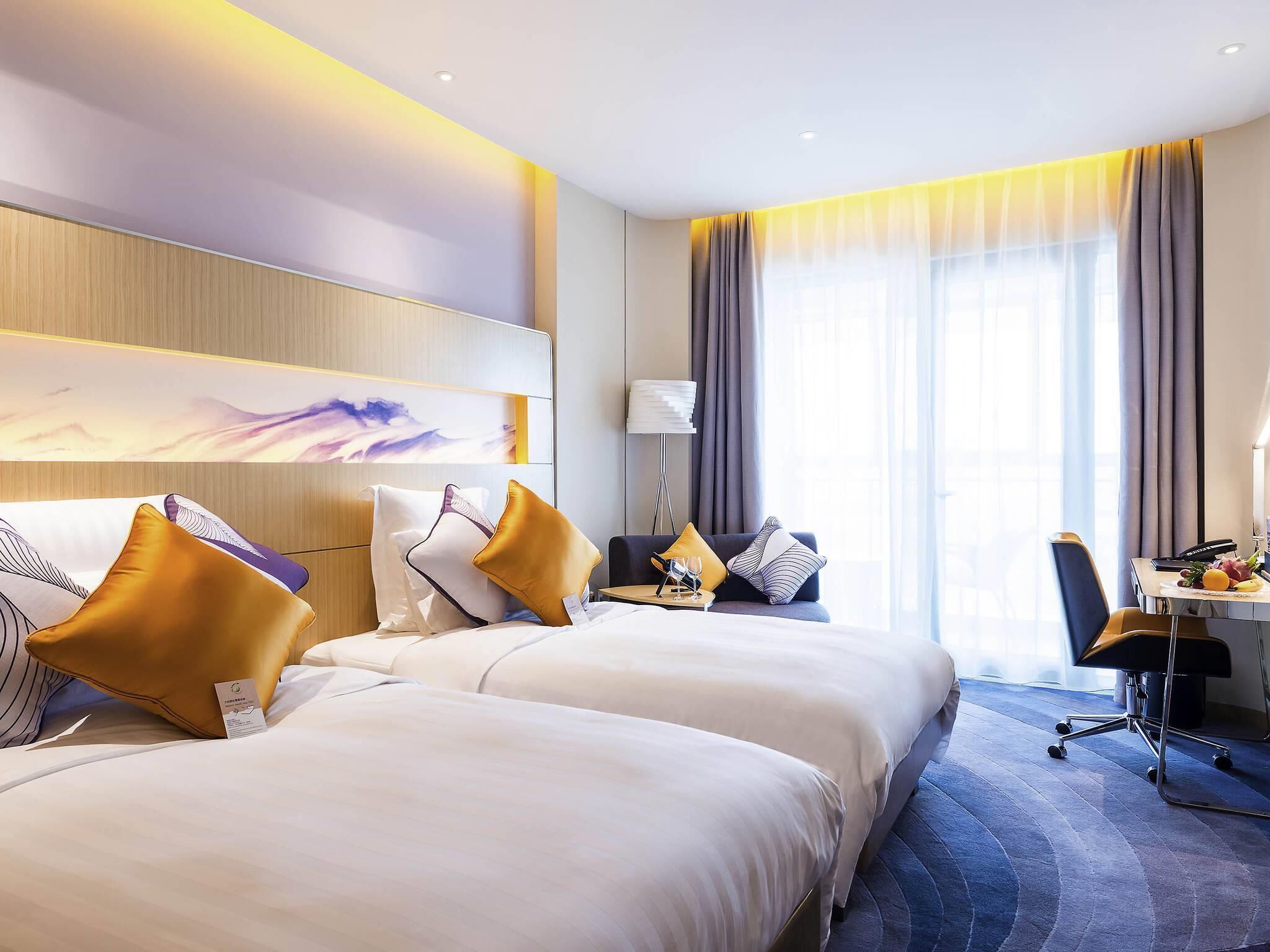 A hotel room with two beds, a desk, a chair, and a large window with curtains.