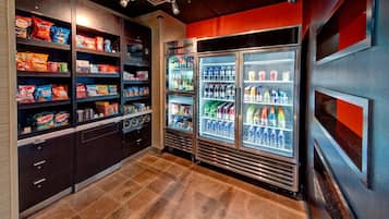 Un mostrador de aperitivos con estantes llenos de papas fritas y bocadillos, y un refrigerador con agua embotellada y jugos.