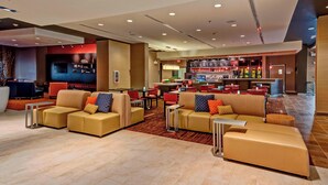 Een moderne hotellobby met leren banken, een bar en een televisiescherm.