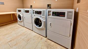 A laundry facility with four washing machines and dryers, a bench, and a sign with operating instructions.