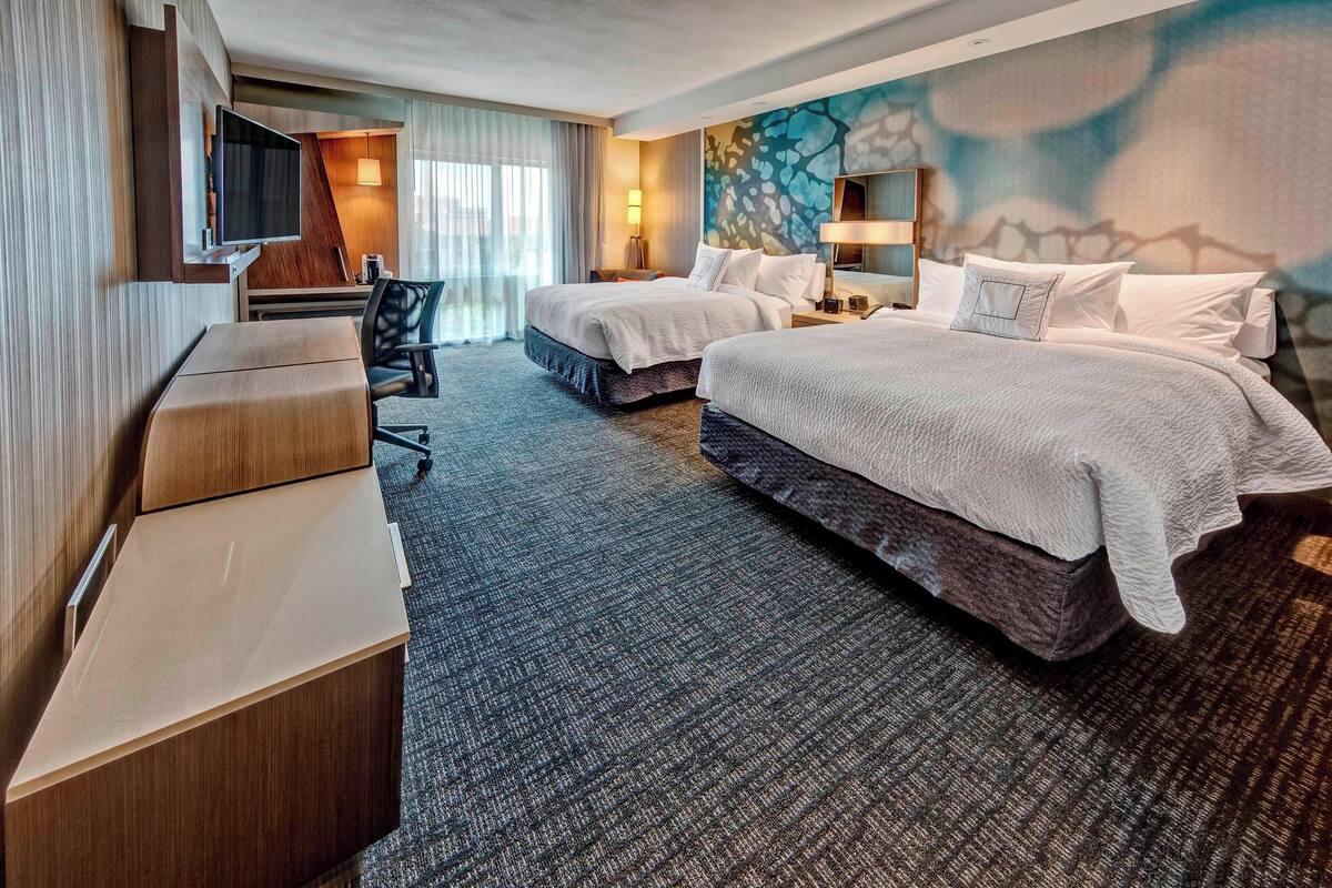 Hotelkamer met twee bedden, een bureau, een stoel, een televisie en een groot abstract wandtapijt.