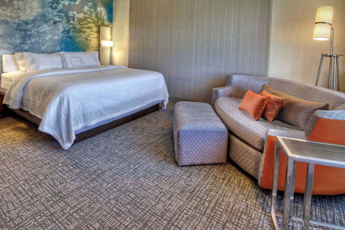Een hotelkamer met een bed, een bank, een tafeltje en een vloerlamp.