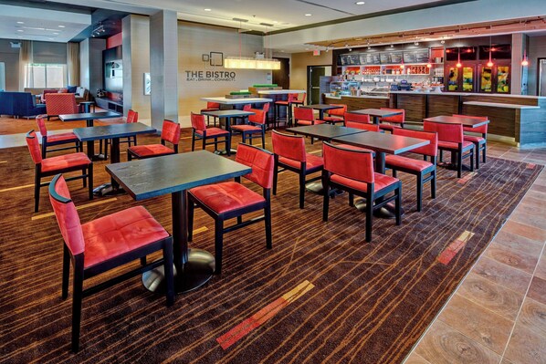 Ein modernes Bistro mit mehreren Tischen und rot gepolsterten Stühlen, einer Theke mit Speisekarte und einer Sitzecke mit Sofas und einem Fernseher.