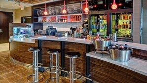 Een bar met een toonbank, krukken, een kassa en verschillende flessen en glazen.