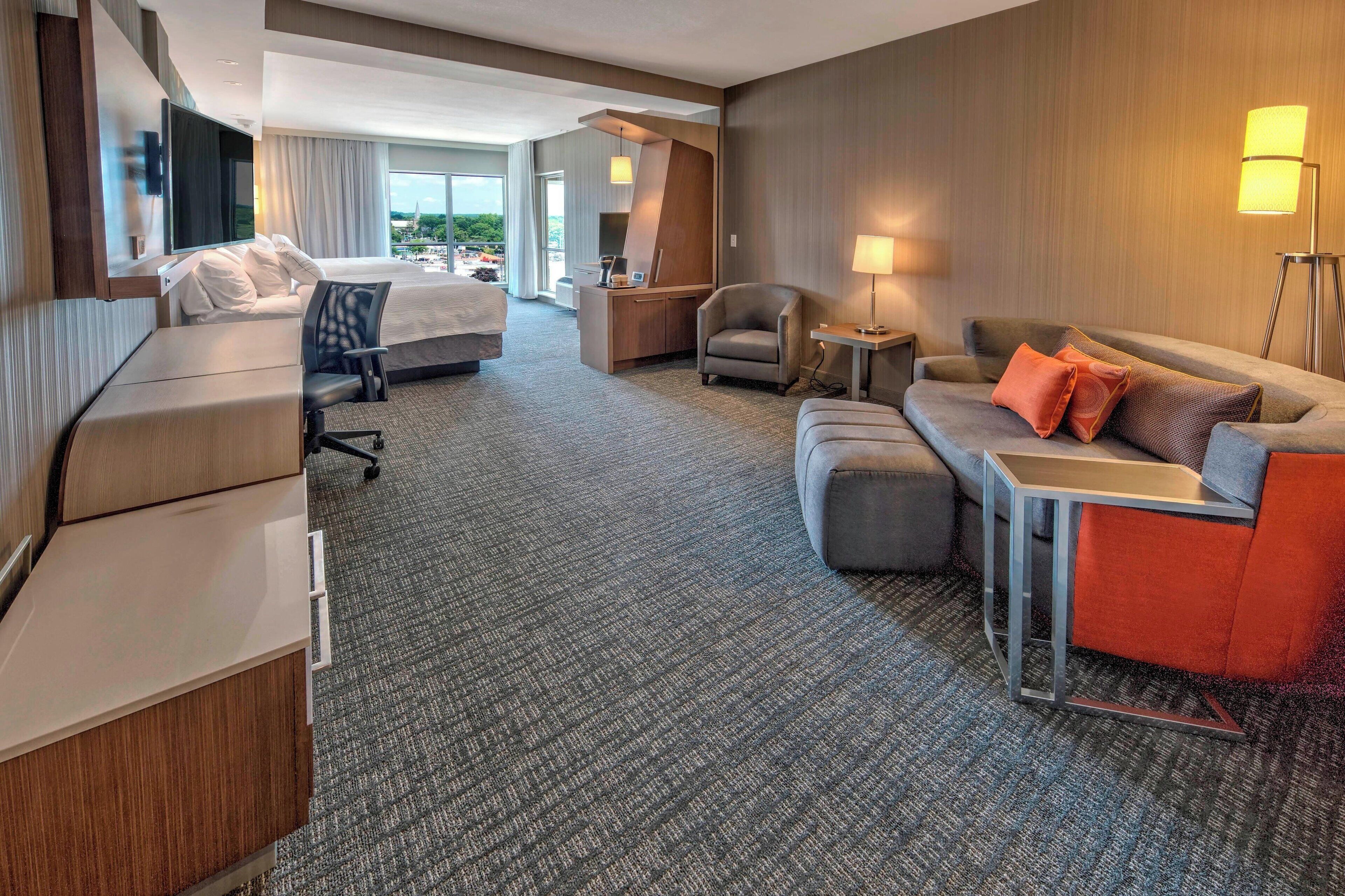 A hotel room with a bed, a desk, a sofa, a chair, and a lamp.