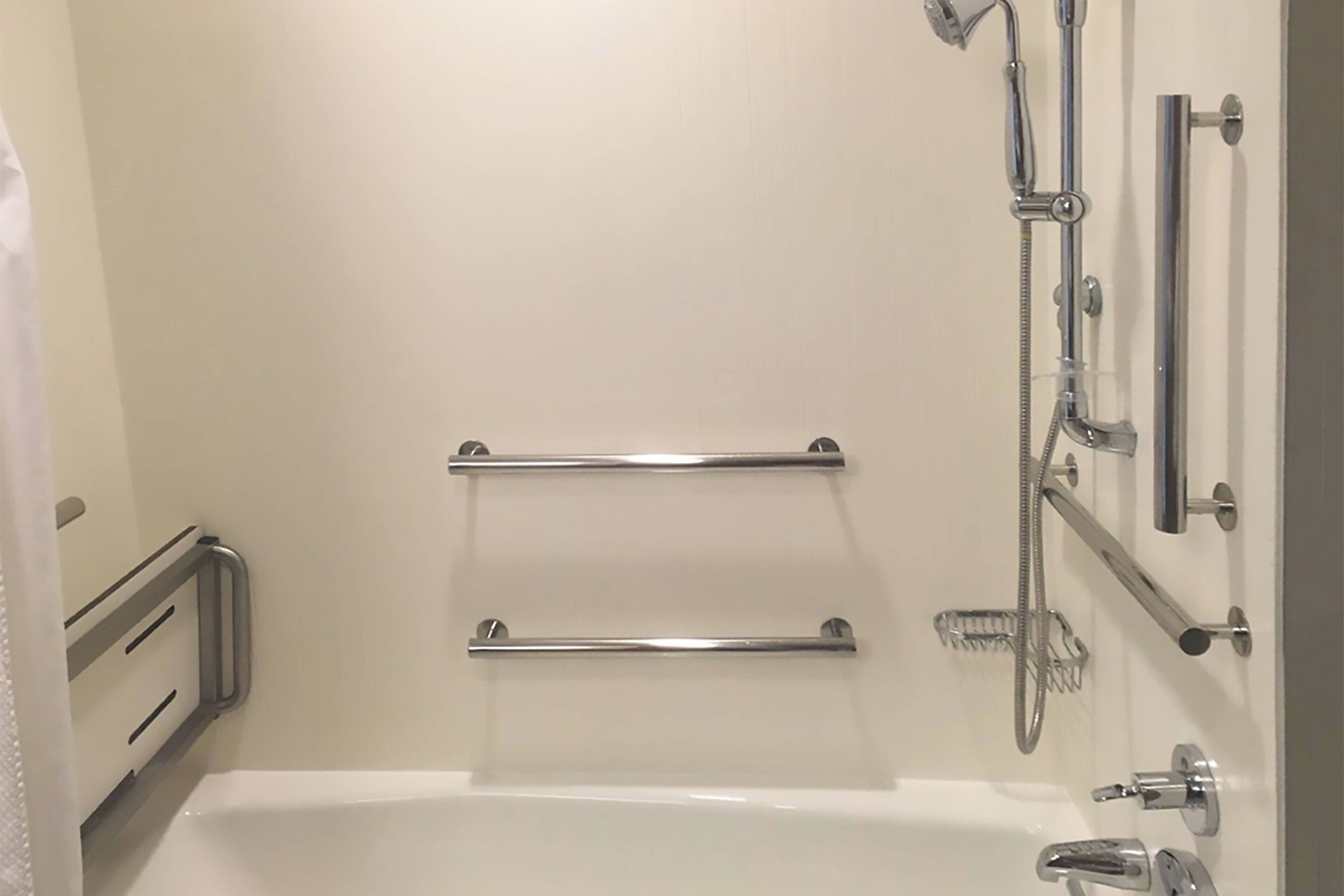 Baño con bañera, dos barras de apoyo, cabezal de ducha y ducha de mano.