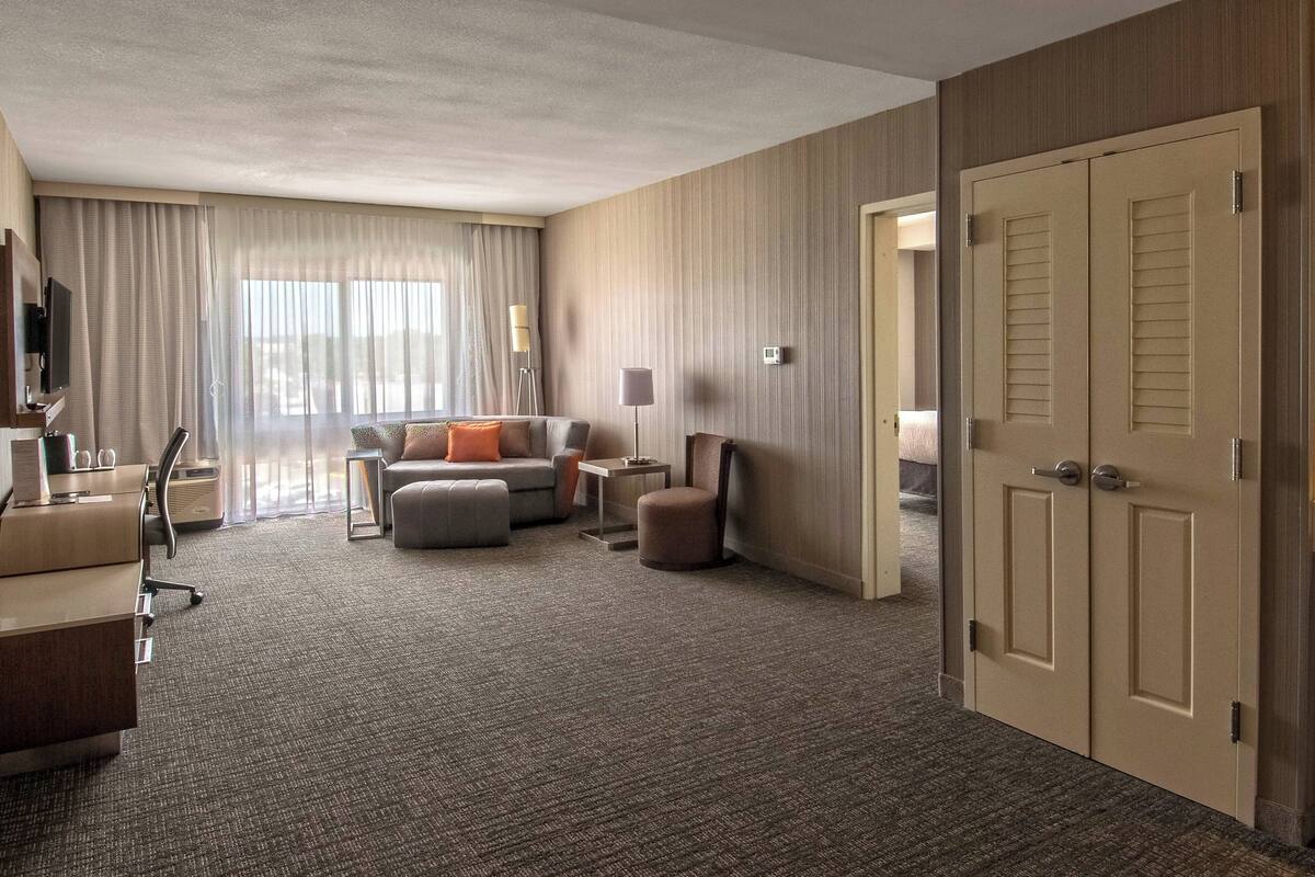 Een hotelkamer met een bank, een poef en een bureau met een lamp.