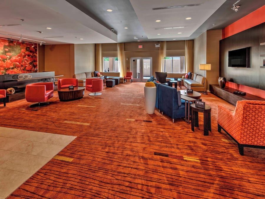 A spacious lobby with a mix of seating options, including sofas and chairs, a reception desk, and a large wall-mounted TV.