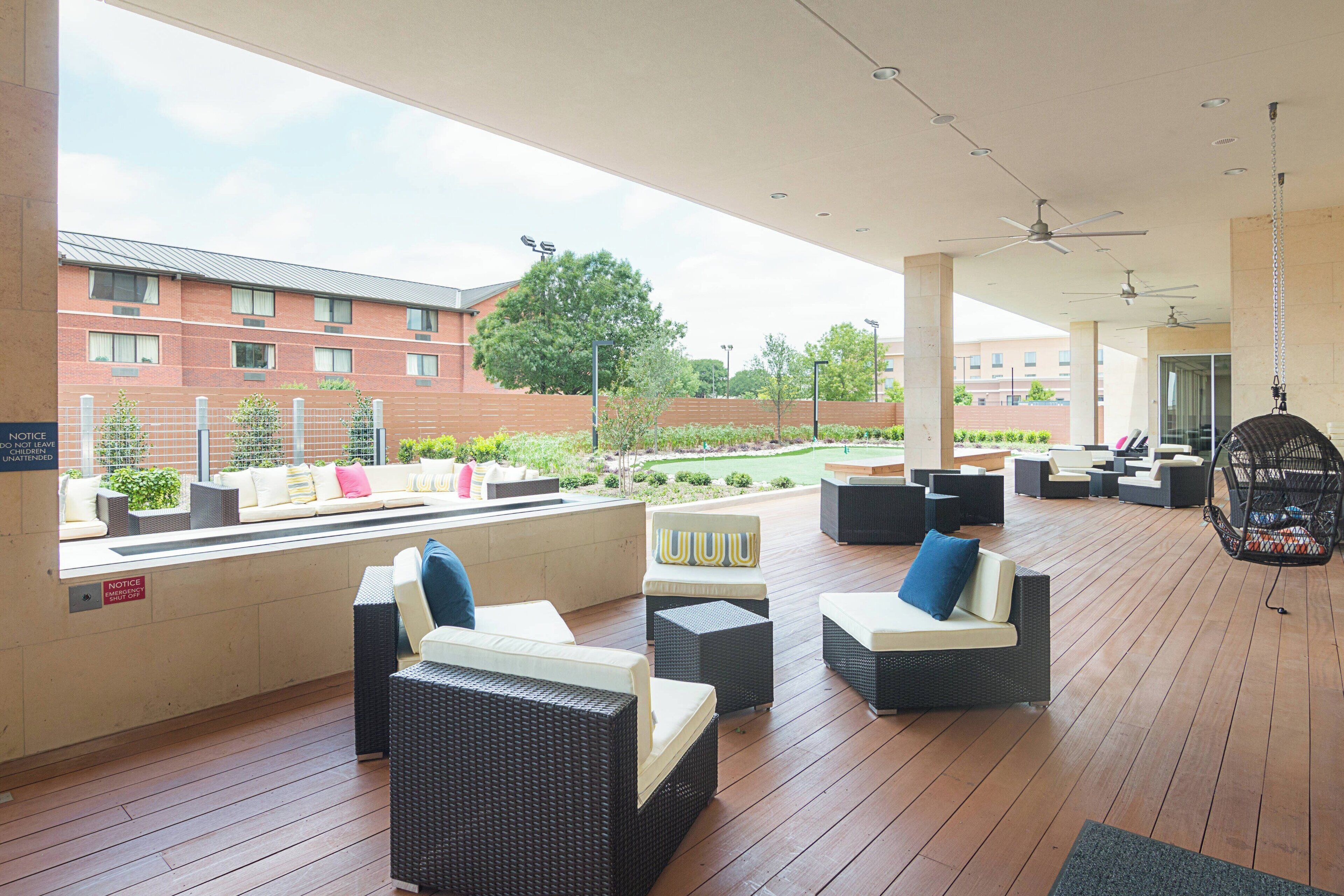 A covered outdoor seating area with wicker furniture and a view of a brick building.