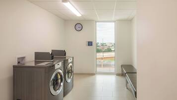 A laundry room with two front-loading washers and dryers, a clock on the wall, and a bench near the door.