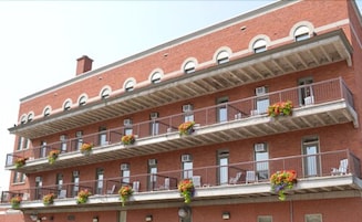 Un edificio de ladrillo de varios pisos con balcones, cada uno decorado con macetas de flores.