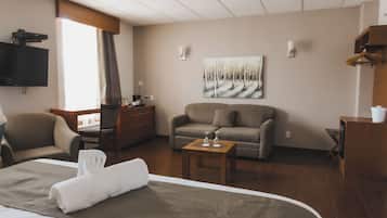 A hotel room with a bed, a sofa, a desk, a television, and a painting on the wall.
