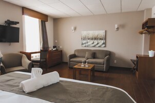Habitación de hotel con cama, sofá, escritorio, televisión y un cuadro en la pared.