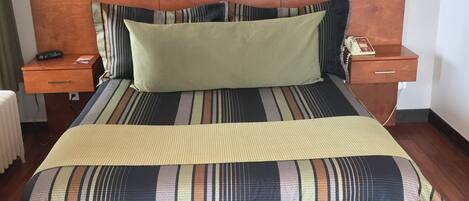 Una cama bien hecha con ropa de cama a rayas, un cabecero de madera y una mesita de noche con una lámpara.