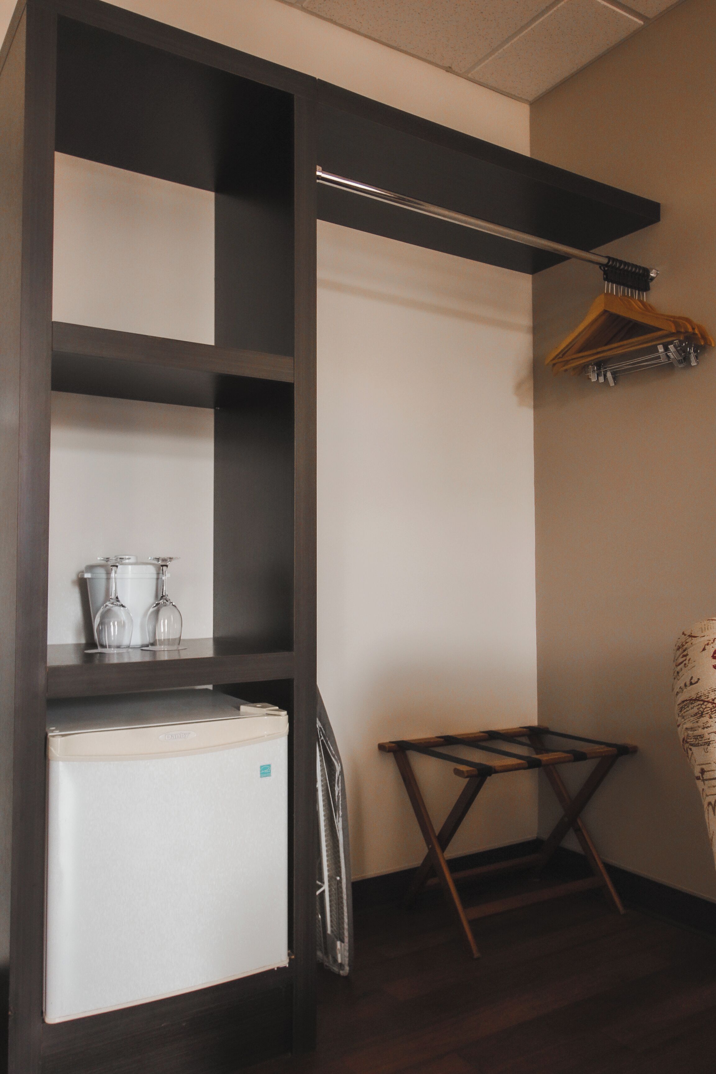 A compact kitchenette with a refrigerator, a small table, and a hanging clothes rack.
