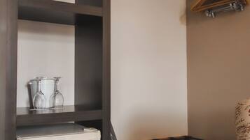 A compact kitchenette with a refrigerator, a small table, and a hanging clothes rack.
