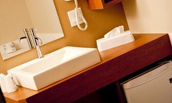 Un baño con un lavamanos blanco, un espejo, un teléfono y una caja de pañuelos.
