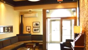 Eine Lobby mit einer Couch, Sesseln, einem Couchtisch, gerahmten Bildern an der Wand und einer Lampe.