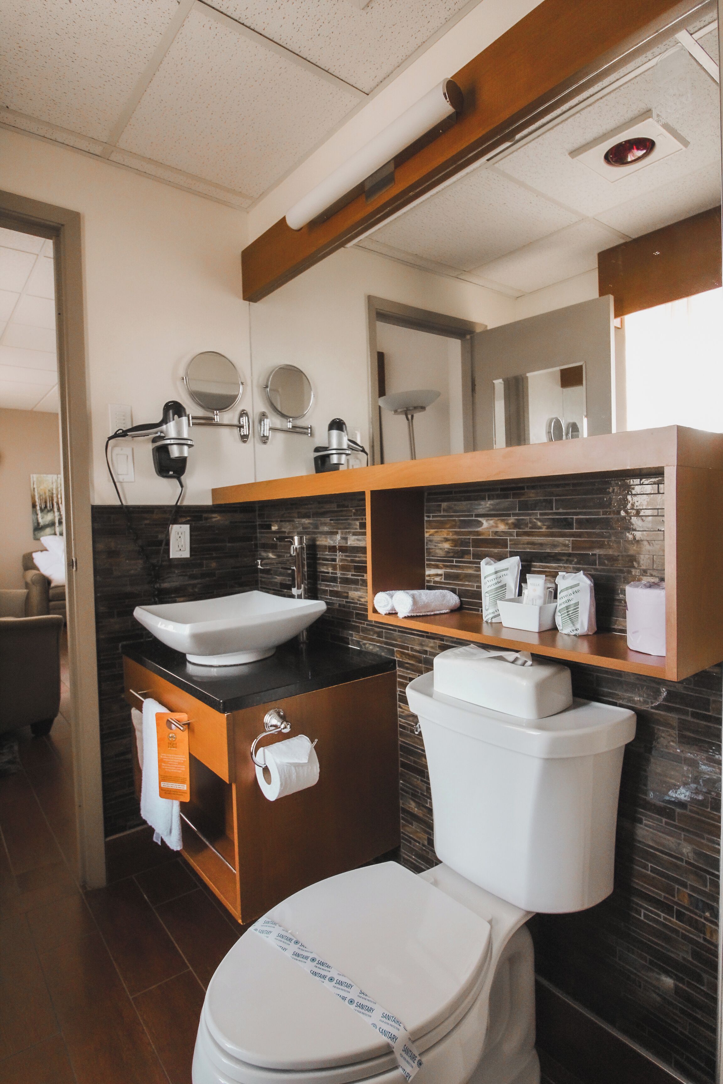 Een moderne badkamer met een wit wastafelmeubel, toilet en een spiegel boven het wastafelmeubel. Er zijn planken met toiletartikelen en een handdoekrek.
