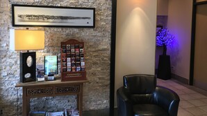 Eine Lobby mit Steinwand, einem gerahmten Bild, einem Tisch mit Lampe, einem Stuhl und einem Hinweisschild.