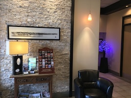 Un vestíbulo con pared de piedra, un cuadro enmarco, una mesa con lámpara, una silla y un cartel.
