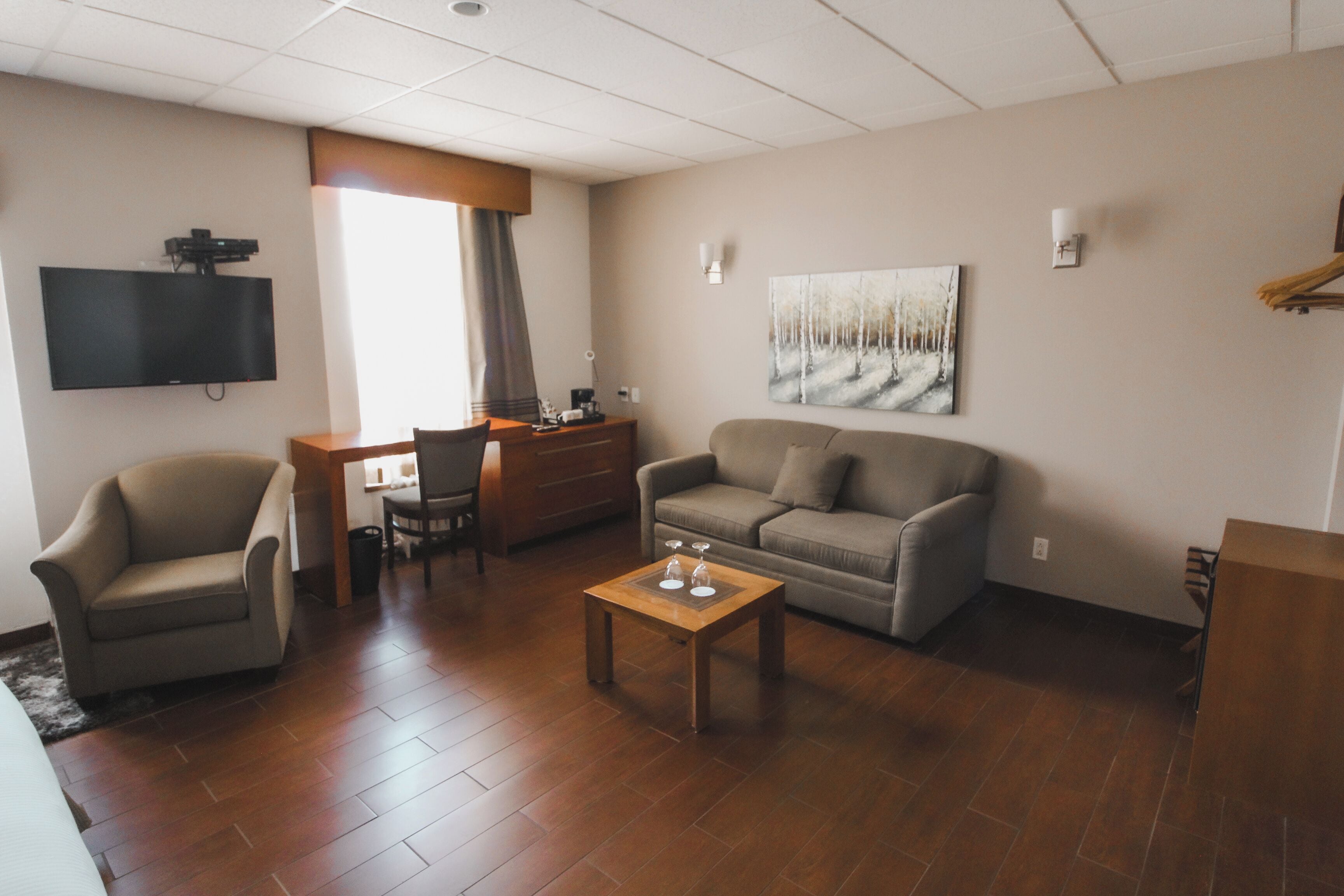 Una sala de estar amoblada con un sofá, un sillón, una mesita de centro y un televisor de pantalla plana montado en la pared.