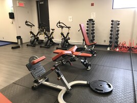 Uma academia com equipamentos de musculação, bicicletas ergométricas e uma porta identificada com a inscrição 'EXIT'.