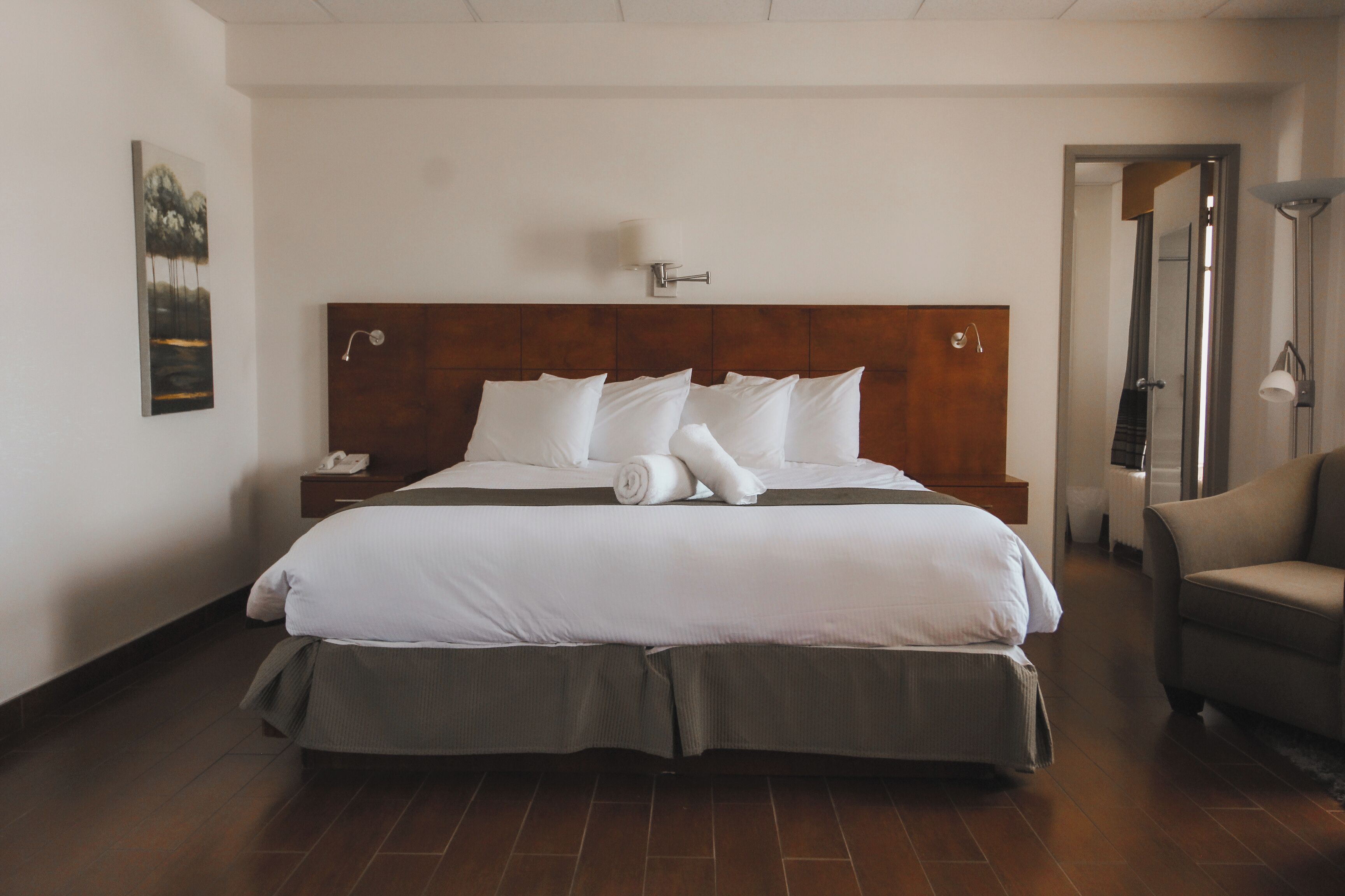 A hotel room with a large bed, a bedside table with a lamp, and a door leading to another room.