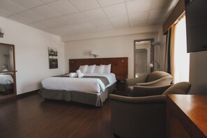 A hotel room with a bed, a chair, a desk, a mirror, and a painting on the wall. - Hôtel du Fjord (Saguenay)