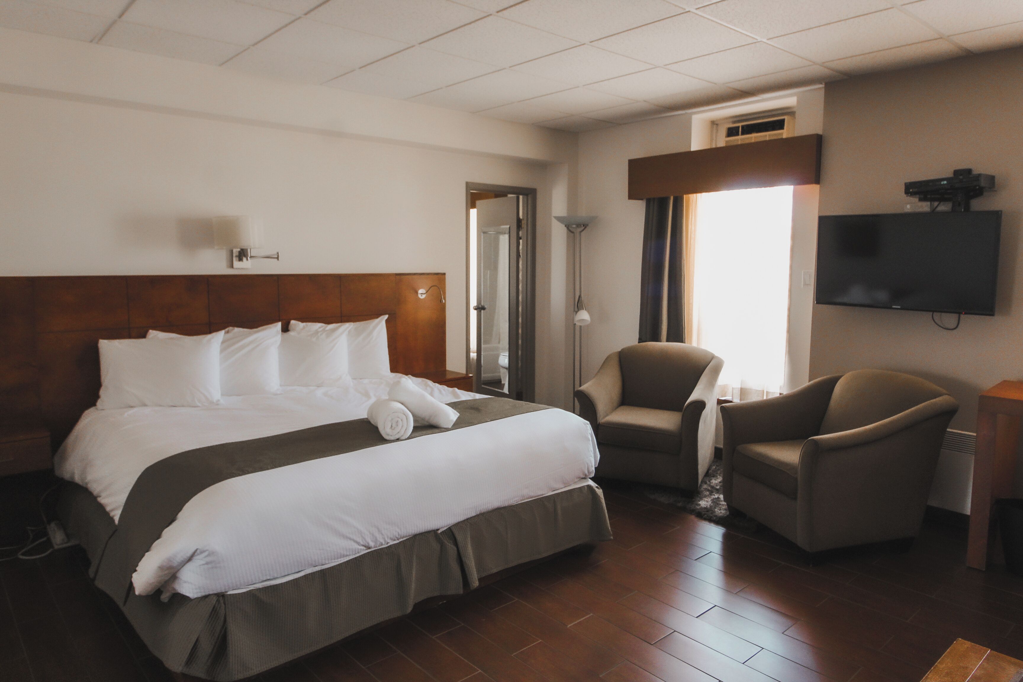 Une chambre d’hôtel avec un grand lit, deux fauteuils, un téléviseur à écran plat et une fenêtre avec des rideaux.