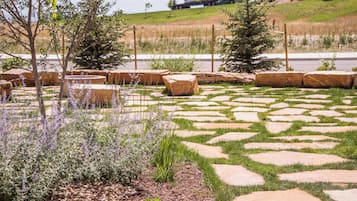 A landscaped garden with stone pathways, various shrubs, and a backdrop of a road with vehicles.