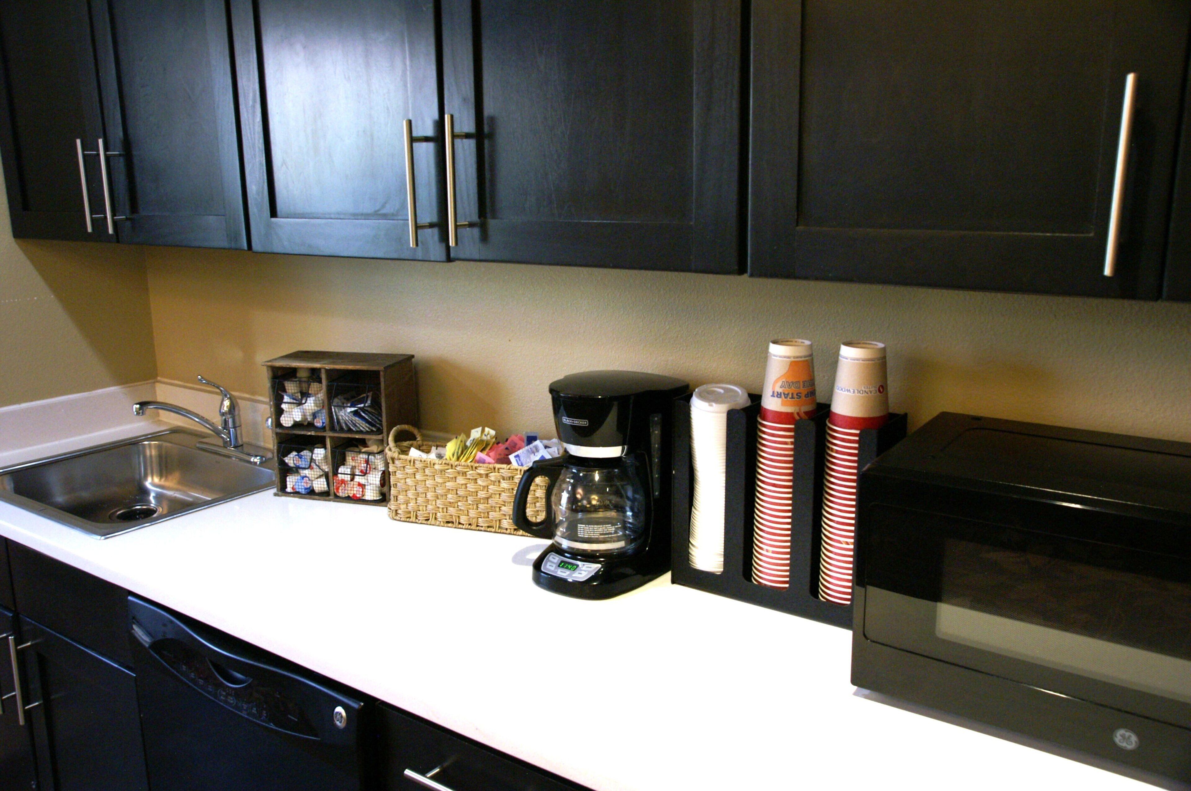 A kitchen with dark cabinets, a coffee maker, a microwave, and a sink.