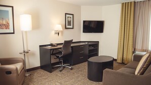 Habitación de hotel con escritorio, dos sillas, televisor y ventana con cortinas.