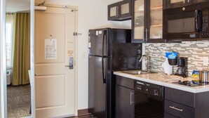 Una cocina compacta con armarios oscuros, un refrigerador, un microondas y una cafetera.