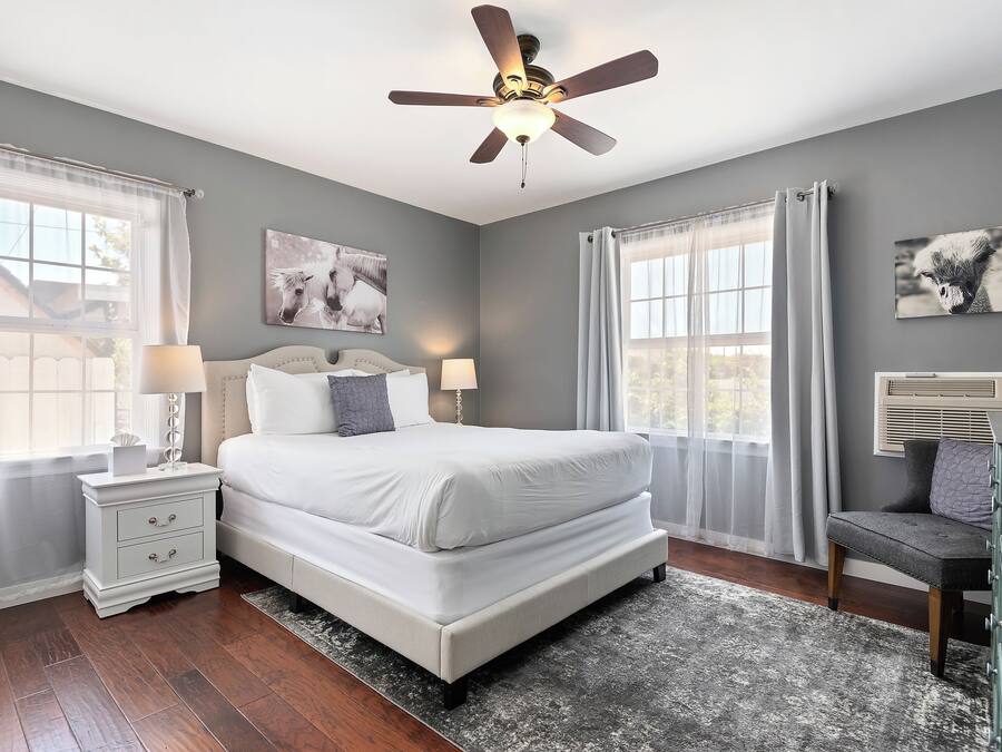 A bedroom with a bed, nightstands, a ceiling fan, and two windows with curtains.
