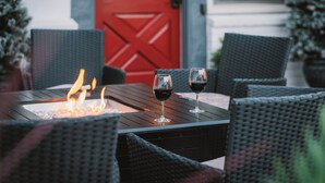 A fire pit table with two glasses of red wine, surrounded by wicker chairs. - New Haven Inn (Solvang)